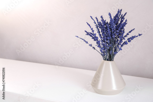 Bouquet of beautiful preserved lavender flowers on white wooden table near beige wall, closeup. Space for text