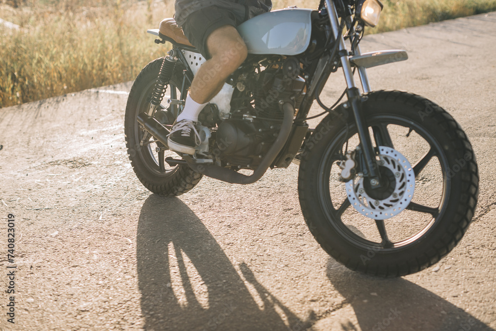 Fototapeta premium Biker on a cafe racer motorcycle on the road at sunset.