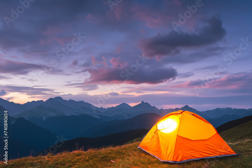 Glowing orange tent in the mountains under dramatic evening sky  mountains in the background. created generative ai