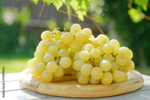Cluster of ripe green grapes on a wooden serving board, backlit by the warm summer sun in a garden setting.