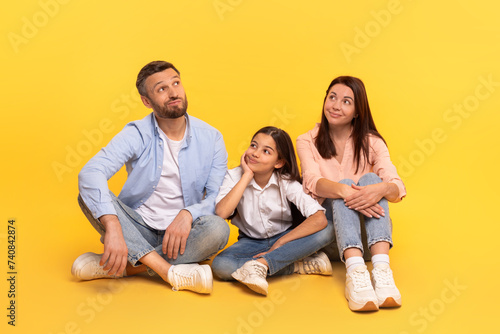 Family of three sitting together with pensive expressions thinking, studio