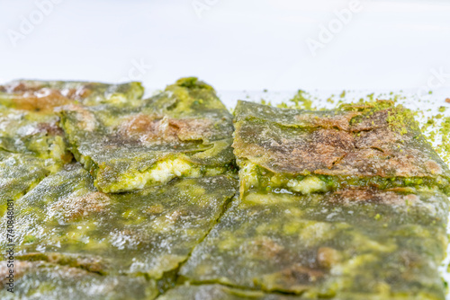 Traditional Turkish dessert Katmer with clotted cream and dough on plate isolated on white background. Prepared with thin dough, green ground pistachio and sherbet. Dessert of Gaziantep region.