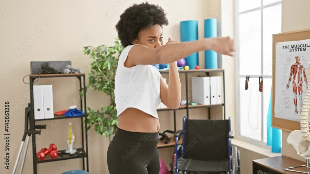 A focused woman boxing in a gym with exercise equipment and educational anatomy posters in the background. A focused woman boxing in a gym with exercise equipment and educational anatomy posters in the background.