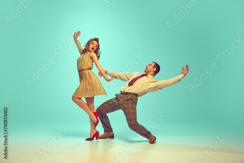Two dancers, man and woman dressed retro outfits in mid-twirl, embodying 50s swing dance enthusiasm against gradient mint background. Concept of music, energy, art, happiness, mood, action photo