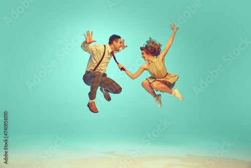 Portrait of modern jazz-dancers in mid-air against gradient mint background. Joyful dance partners performing dance. Vintage fashion. Concept of music, energy, happiness, mood, action