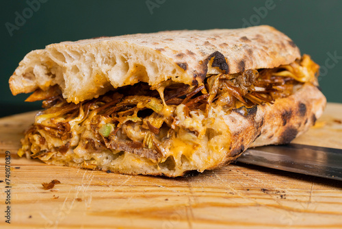 Panuozzo tradizionale di gragnano con carciofi fritti, cheesesteak e formaggio fuso tagliato a metà e servito su un tagliere di legno in un pub