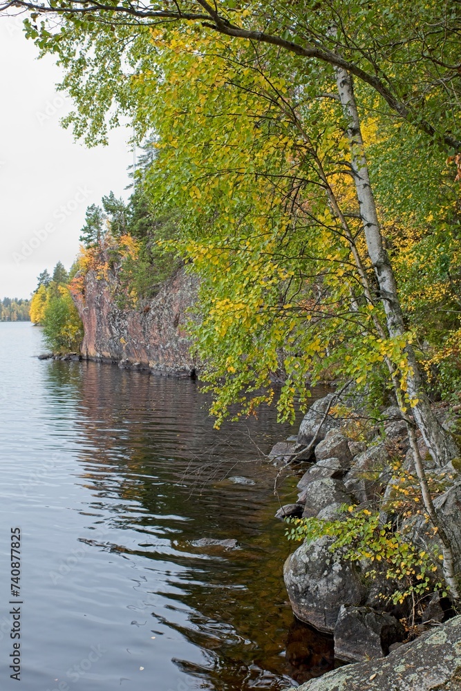 View of lake shore with trees and bluff in cloudy autumn weather.