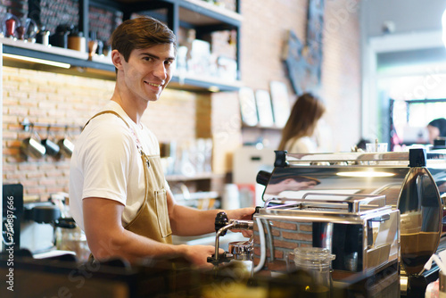 Professional young coffee barista standing inside the counter bar in the coffee shop and making arms crossed and looking at camera  handsome - good looking caucasian ethnic barista posing.