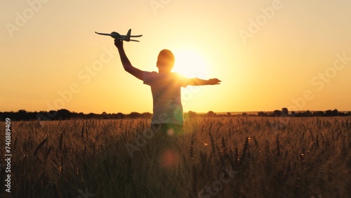 Cheerful boy teen running with plane toy on autumn wheat field at cinematic sunset sunrise back view closeup. Active male kid playing flying airplane plaything enjoy freedom happy childhood at meadow photo