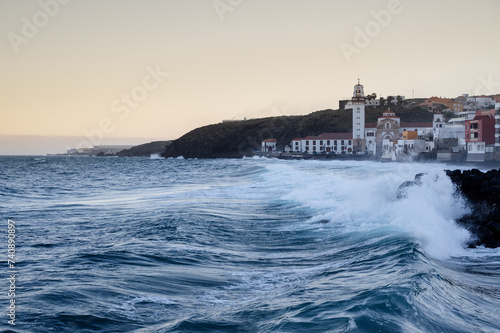 Waves breaking next to its coastal village in the background the church of Candelaria in Tenerife