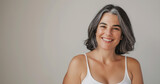 Studio portrait of happy and attractive mature woman with gray hair, smiling and wearing white tank top