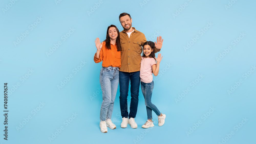 Happy family of three waving hands embracing over blue background