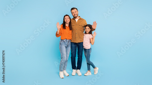 Happy family of three waving hands embracing over blue background © Prostock-studio