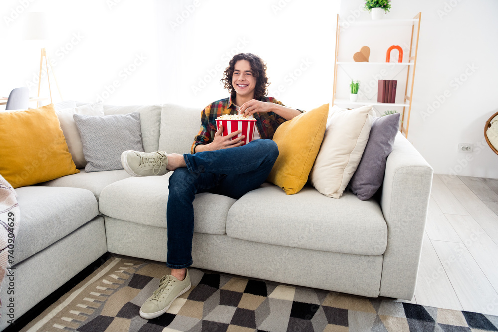 Full length photo of good mood funky guy dressed checkered shirt enjoying pop corn watching tv indoors house home room Full length photo of good mood funky guy dressed checkered shirt enjoying pop corn watching tv indoors house home room