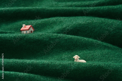 Miniature Homestead on Woolen Pasture. Tiny sheep and house figurines on a green wool fabric depicting a pastoral scene. photo