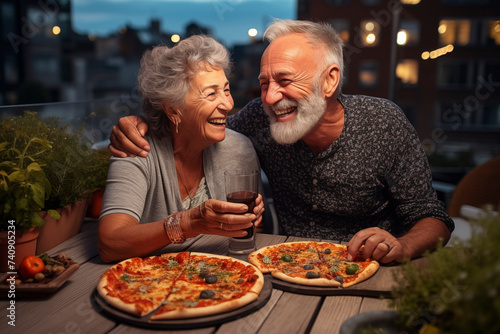 Happy senior old couple have fun eating a pizza together outdoor in traditional italian pizzeria restaurant sitting and talking and laughing. People enjoying food and elderly lifestyle. Retirement