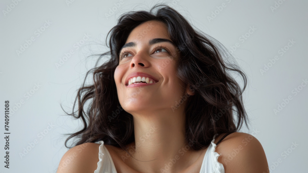 joyful woman with shoulder-length curly hair, looking upwards with a bright smile, wearing a tank top, against a light background. joyful woman with shoulder-length curly hair, looking upwards with a bright smile, wearing a tank top, against a light background.