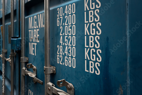 Shallow focus of a generic, standing shipping container showing weight measurements on one of the metal doors. The metal bar locks are clearly visible.