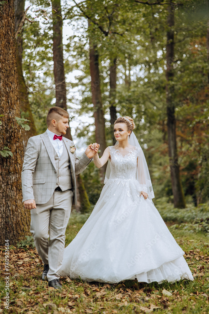 A wedding couple is walking in nature on an autumn day. Happy young bride and elegant groom holding hands. A stylish couple of newlyweds on their wedding day.