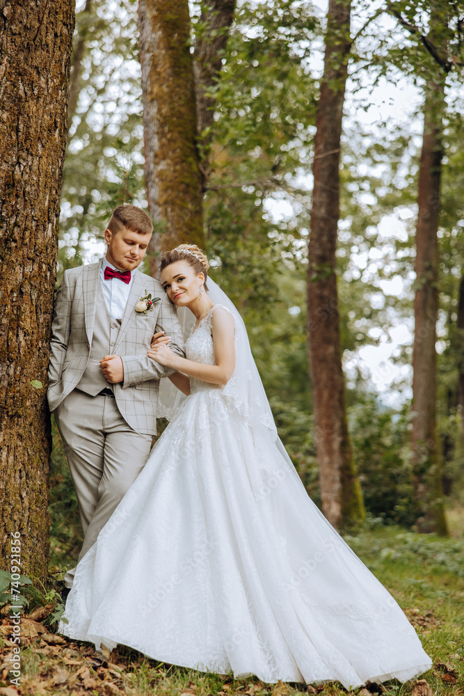 lovely and stylish newlyweds are hugging and smiling against the background of autumn nature in a beautiful garden. An incredibly beautiful young bride leaned against the shoulder of her beloved groom lovely and stylish newlyweds are hugging and smiling against the background of autumn nature in a beautiful garden. An incredibly beautiful young bride leaned against the shoulder of her beloved groom