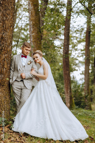 lovely and stylish newlyweds are hugging and smiling against the background of autumn nature in a beautiful garden. An incredibly beautiful young bride leaned against the shoulder of her beloved groom © Vasil
