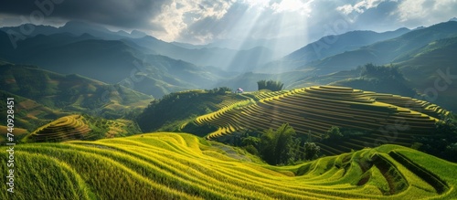 The sun breaks through the clouds, casting light over the lush green hillside, creating a picturesque natural landscape with mountainous landforms