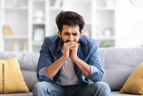 Sorrow And Grief. Depressed young indian man sitting on sofa at home © Prostock-studio