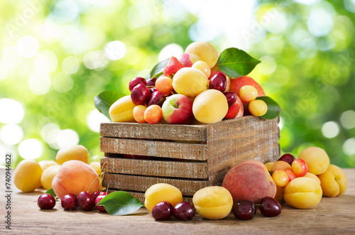 Mix of fresh fruits in a wooden box on green background