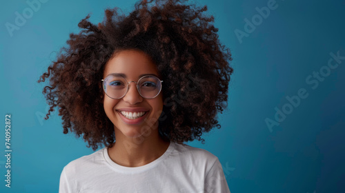 A smiling person with glasses and voluminous hair radiates joy against a solid blue background.
