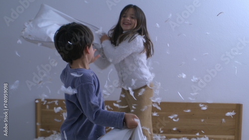 Happy siblings having fun with pillow fight, feathers flying in the air, children engaged in carefree joyful play captured in super slow motion