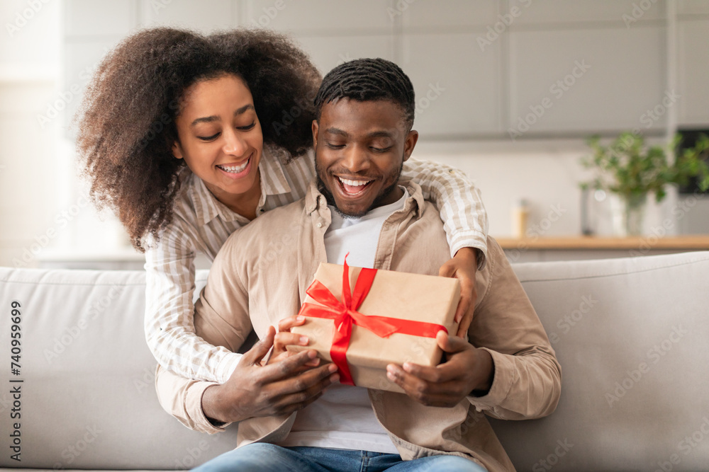 Young joyful black couple celebrating holidays woman presenting gift indoors Young joyful black couple celebrating holidays woman presenting gift indoors