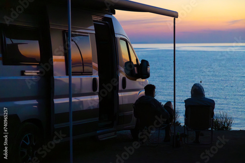 a couple sitting in front of a campervan on the seashore at sunset
