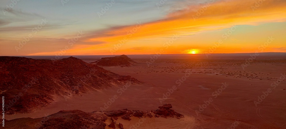 Panoramic sunset view from Timimoun, Algeria, overlooking the red sand desert and canyons from a hilltop.