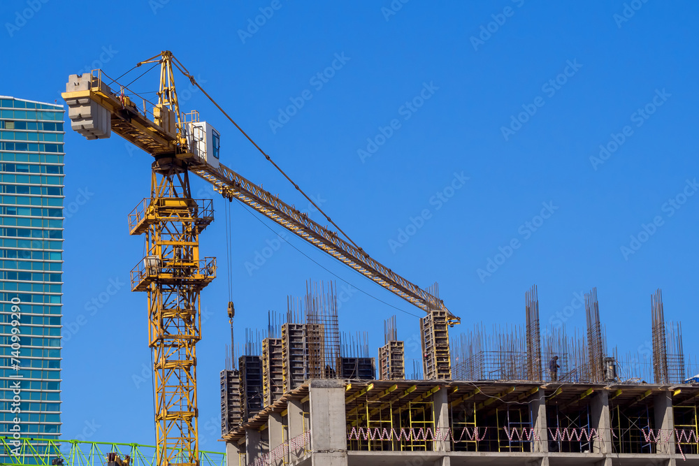 Yellow tower crane on construction site against blue sky background to illustrate construction, urban development and progress Yellow tower crane on construction site against blue sky background to illustrate construction, urban development and progress