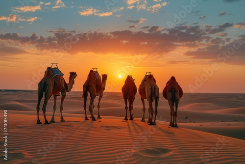 Group of camels standing together on sand dunes against a stunning sunset backdrop, with a serene desert landscape.