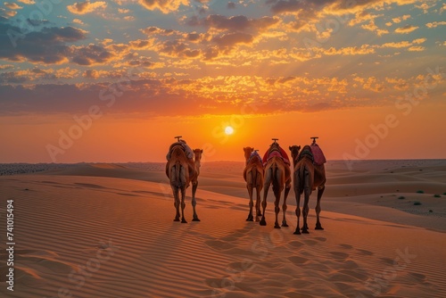 Group of camels standing together on sand dunes against a stunning sunset backdrop, with a serene desert landscape.