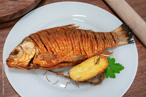 Fried crucian fish on wooden table garnished with potato.