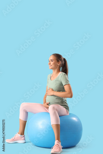 Sporty pregnant woman with fitball training on blue background