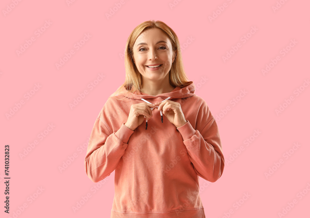 Mature woman in orange hoodie making heart gesture on pink background Mature woman in orange hoodie making heart gesture on pink background