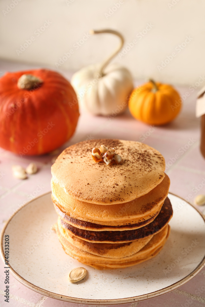 Plate of tasty pumpkin pancakes with cocoa powder, nuts and seeds on pink tile table Plate of tasty pumpkin pancakes with cocoa powder, nuts and seeds on pink tile table