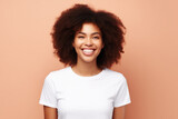 Portrait of a young black woman, happy, smiling. In a white short-sleeved T-shirt on a soft peach background with an empty space
