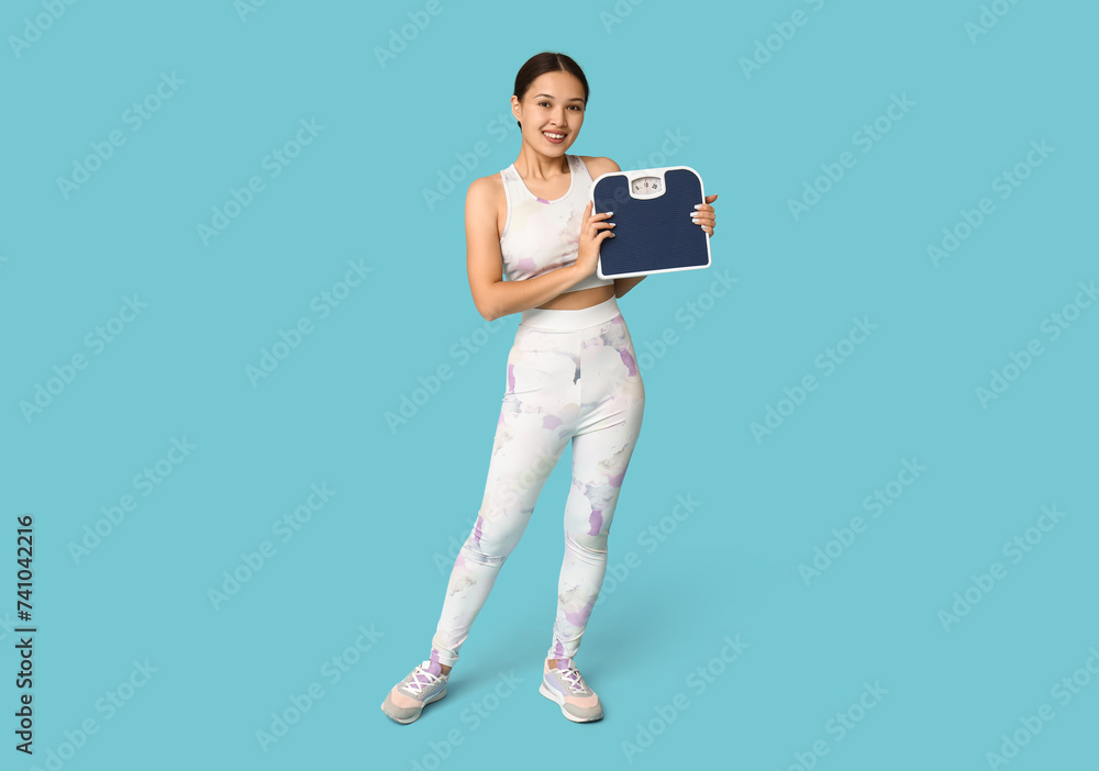 Young woman in sportswear and with weight scales on blue background. Slimming concept