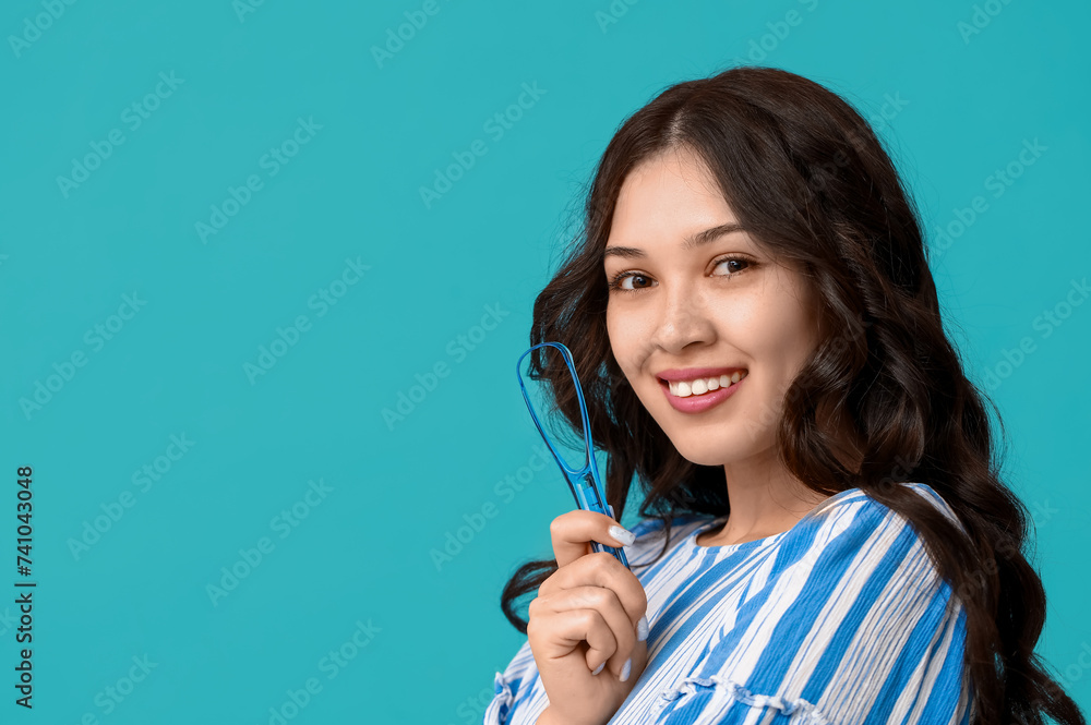 Happy young Asian woman with tongue scraper on blue background Happy young Asian woman with tongue scraper on blue background