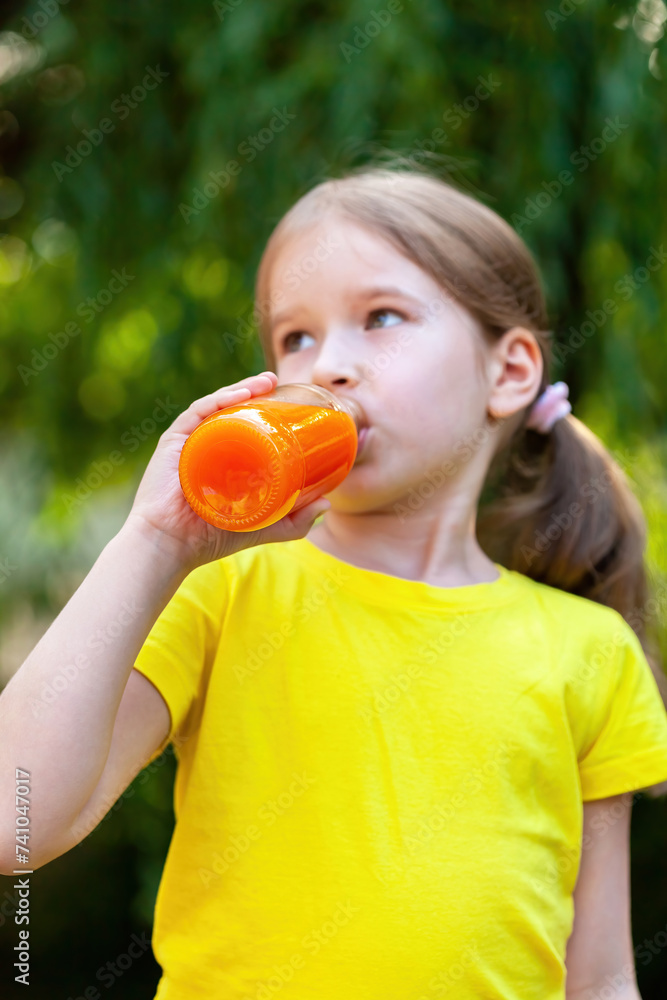 Young girl in a vibrant yellow t-shirt outdoors enjoying a refreshing drink from a clear bottle filled with orange carrot juice. Natural daylight, casual relaxed real lifestyle shot, vertical comp Young girl in a vibrant yellow t-shirt outdoors enjoying a refreshing drink from a clear bottle filled with orange carrot juice. Natural daylight, casual relaxed real lifestyle shot, vertical comp