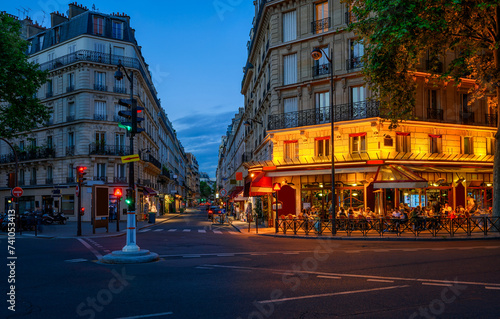 Cozy street with tables of cafe in Paris, France. Night cityscape of Paris. Architecture and landmarks of Paris.