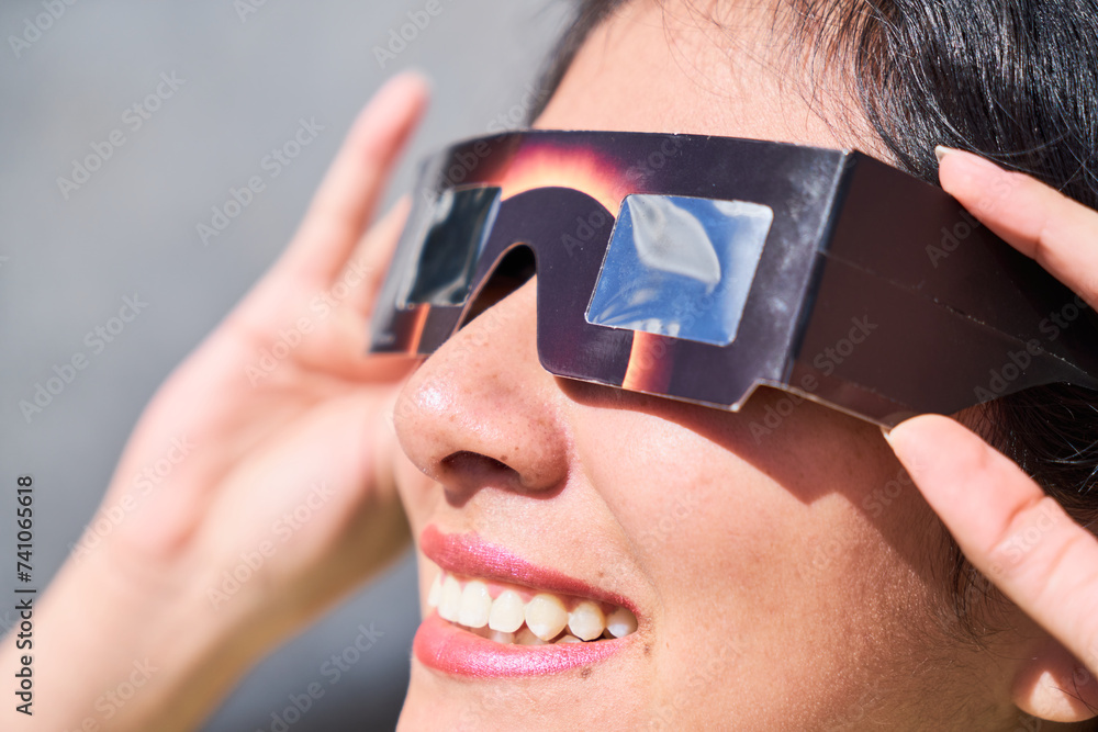 Smiling young latin woman watching an eclipse of the sun with eclipse glasses - obrazy, fototapety, plakaty 