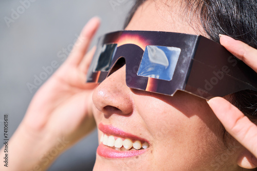 Smiling young latin woman watching an eclipse of the sun with eclipse glasses photo