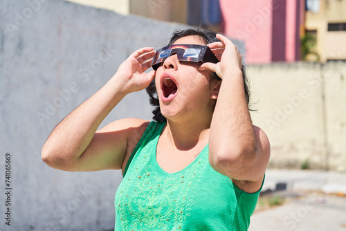 Happy young latina woman with solar eclipse glasses, watching a solar eclipse photo