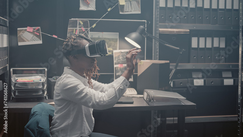 Young investigator using 3d vr headset in incident room, using interactive virtual reality glasses to uncover new clues. Police agent checking forensic evidence and doing detective work.