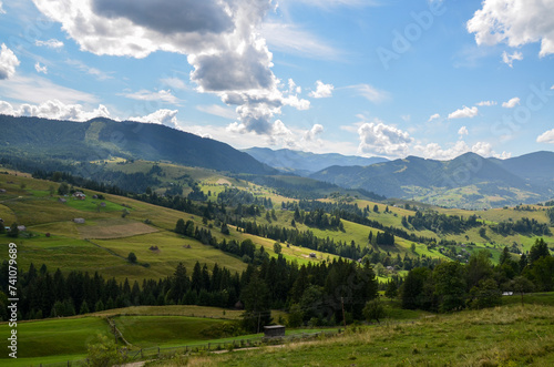 Mountain landscape with green meadows located among dense forests and high mountains, small houses scattered on the green slopes of the hills. Carpathians, Ukraine